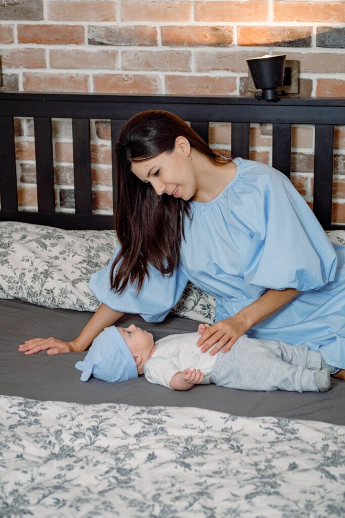 A young beautiful brunette mother singing to her baby son laying on a bed. Maternity, baby care.