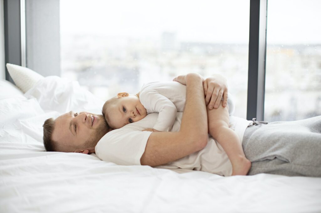 Adorable baby girl cuddling gently to father on white bed