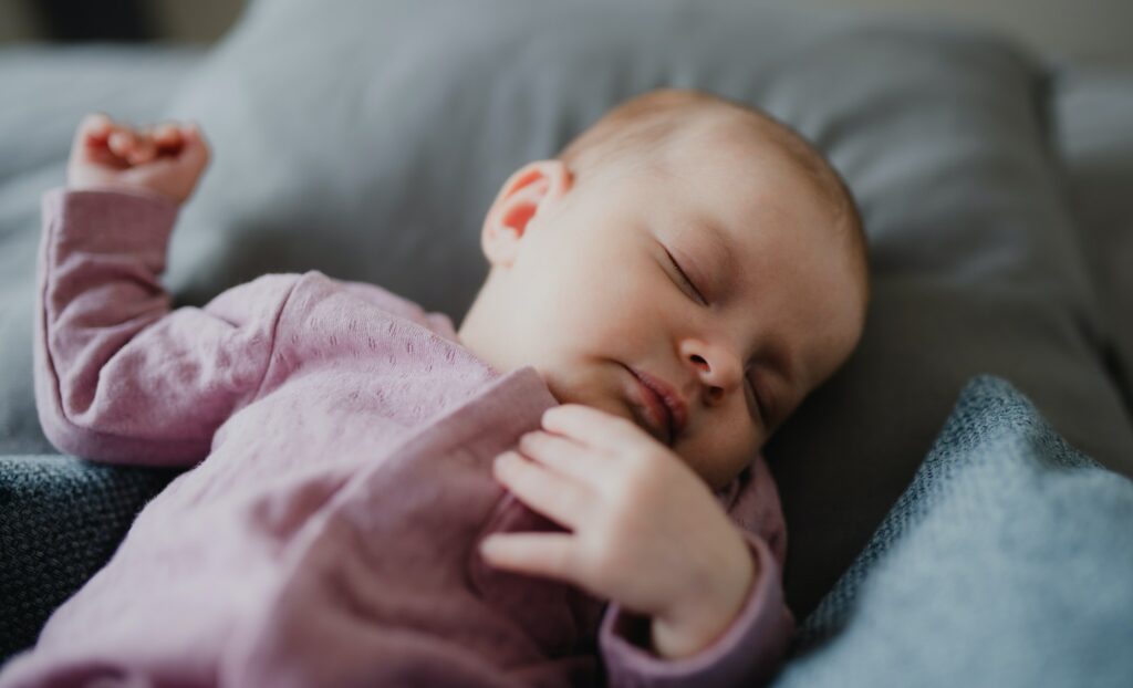 CLose up of cute newborn baby girl, sleeping an lying on sofa indoors at home