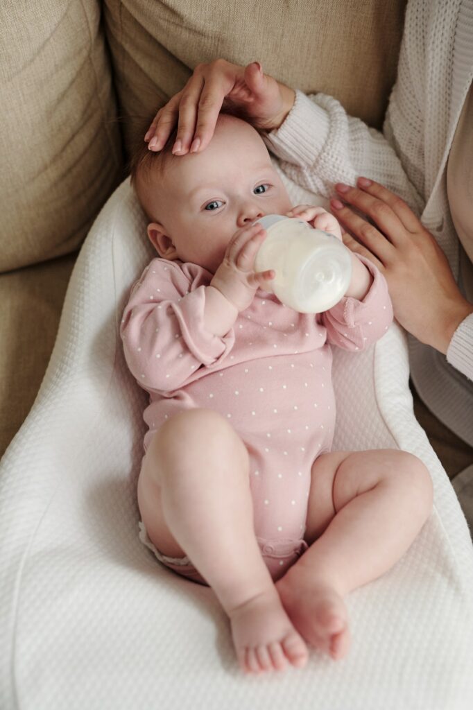 Cute baby girl holding bottle with milk while eating