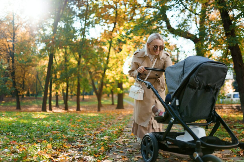 Mother with baby stroller walking in autumn park